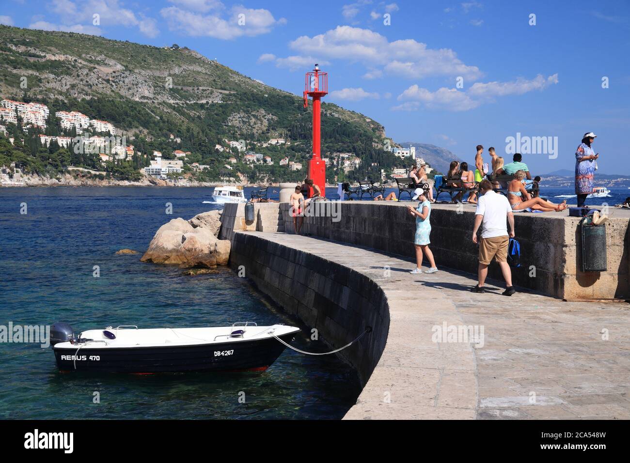 DUBROVNIK, CROACIA - 26 DE JULIO de 2019: Los turistas visitan un rompeolas en el puerto de Dubrovnik, un lugar declarado Patrimonio de la Humanidad por la UNESCO. Foto de stock