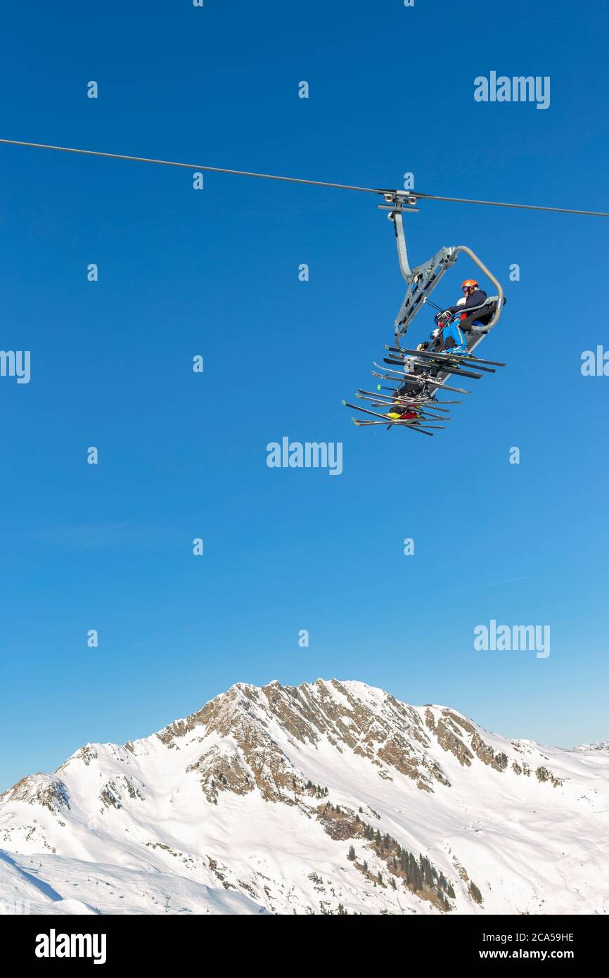 Los esquiadores se sentaron en un telesilla en un día soleado con un cielo azul claro y montañas cubiertas de nieve en el fondo Foto de stock