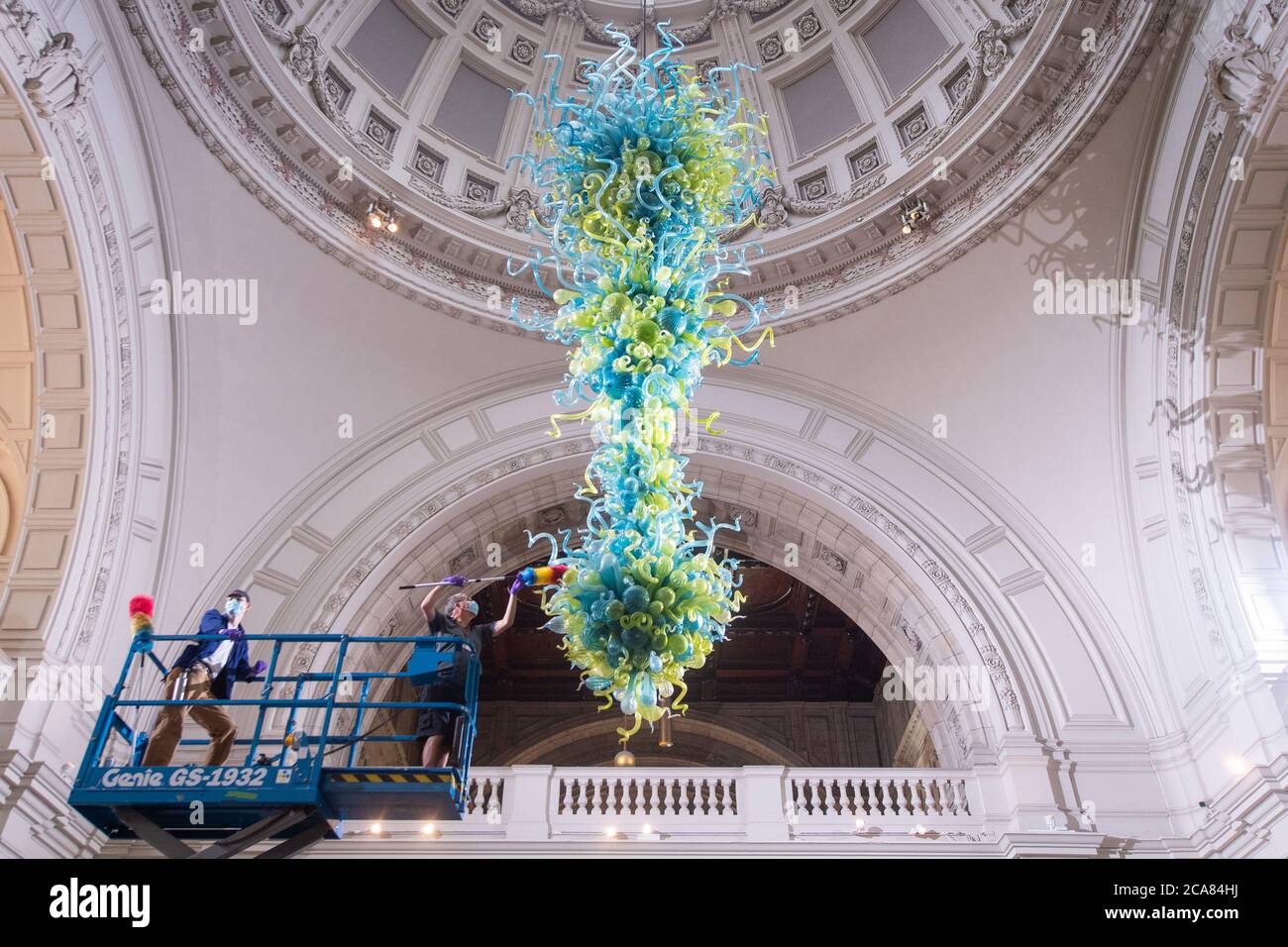 El técnico del museo Andy Monk limpia el vidrio de 27 pies Rotunda Chandelier de Dale Chihuly, que está compuesto por 1,300 elementos de vidrio azul y verde, en el Victoria and Albert Museum en Londres, mientras se prepara para reabrir al público el 6 de agosto. Foto de stock