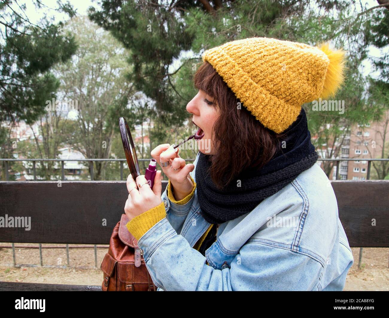 Mujer joven con gorra de lana amarilla sentada en un banco pintando sus  labios frente a un espejo. Concepto urbano de otoño Fotografía de stock -  Alamy