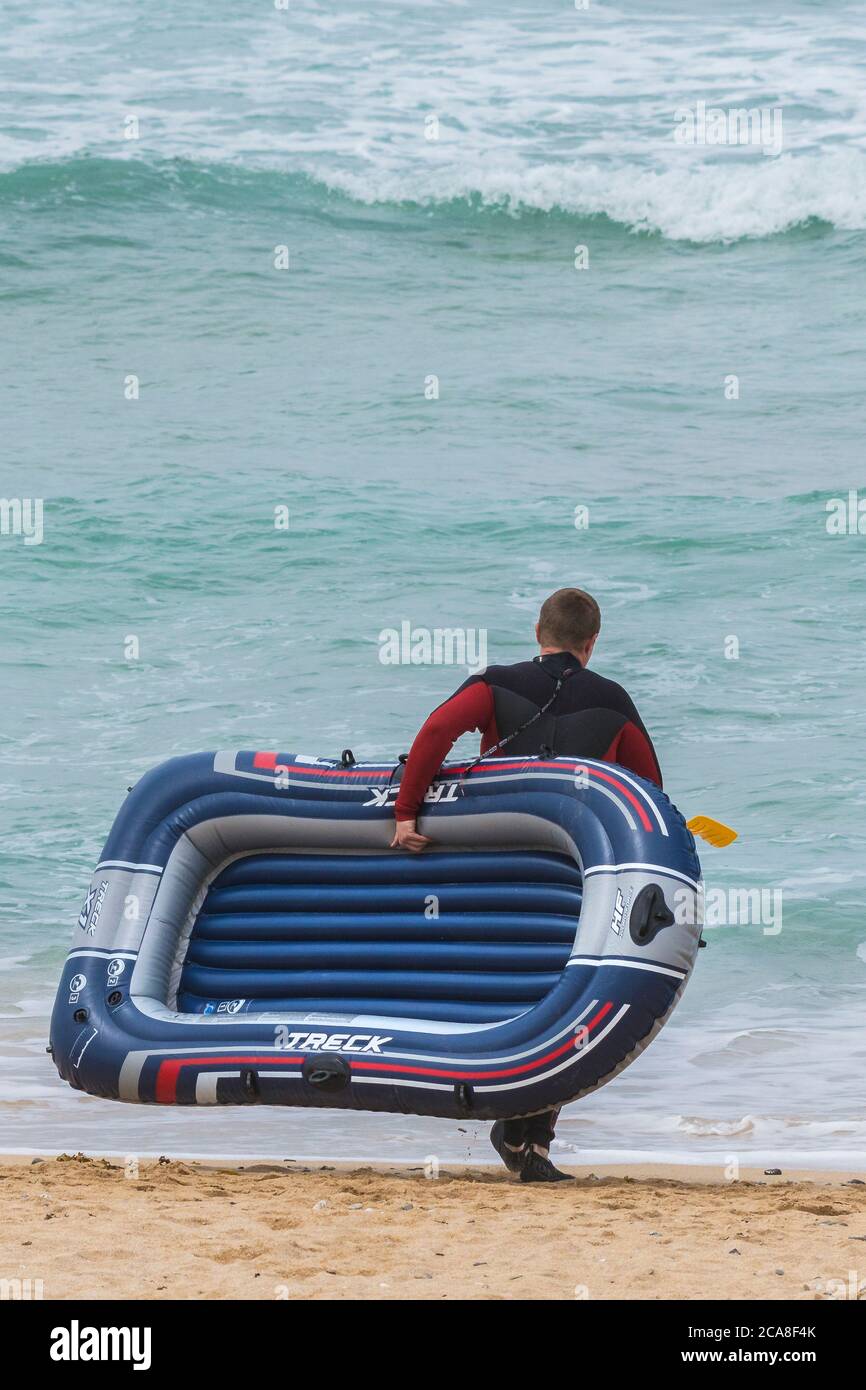 Un veraneante llevando una bote inflable en Fistral; Playa en Newquay en Cornwall. Foto de stock