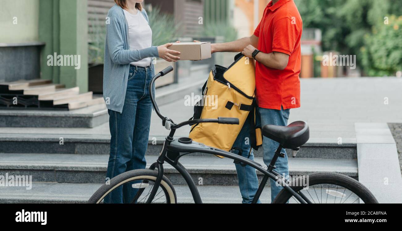 Shopaholic y entrega en línea. Mensajero de bicicletas con mochila y bicicleta da caja de cartón al cliente Foto de stock