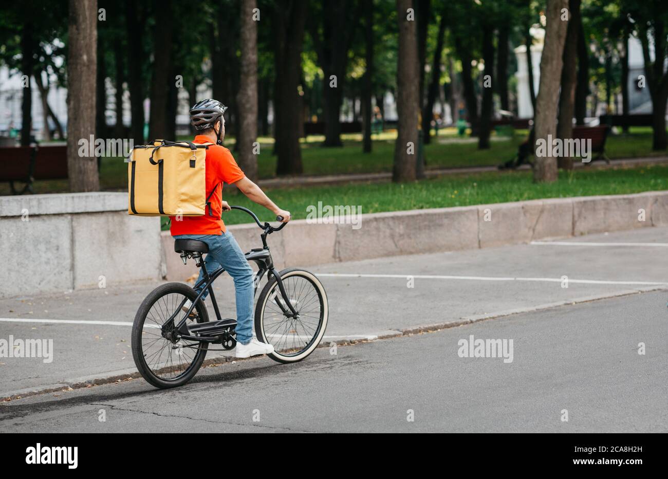 Entrega a la ciudad. Courier en casco con mochila grande paseos en bicicleta Foto de stock