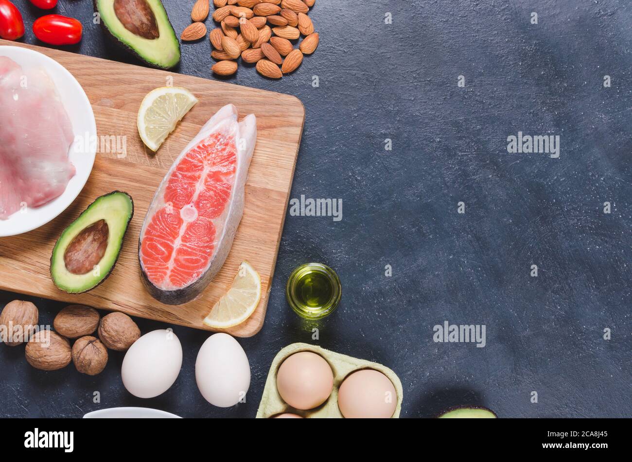 Dieta Keto, comida sana baja en carbohidratos, aguacate, pescado, aceite, nueces sobre fondo negro Foto de stock