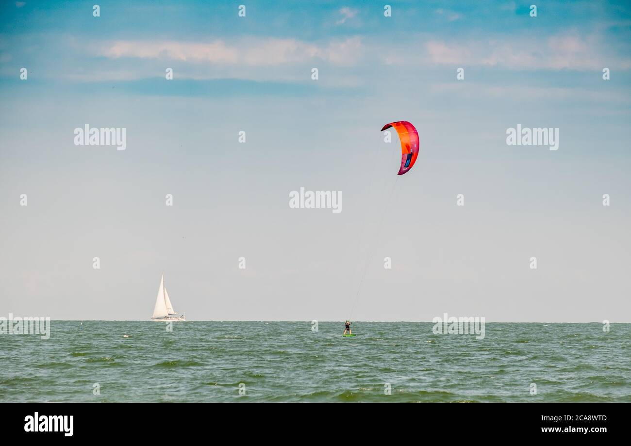 hombre en windsurf con vela roja en el mar azul, en el fondo velero blanco Foto de stock