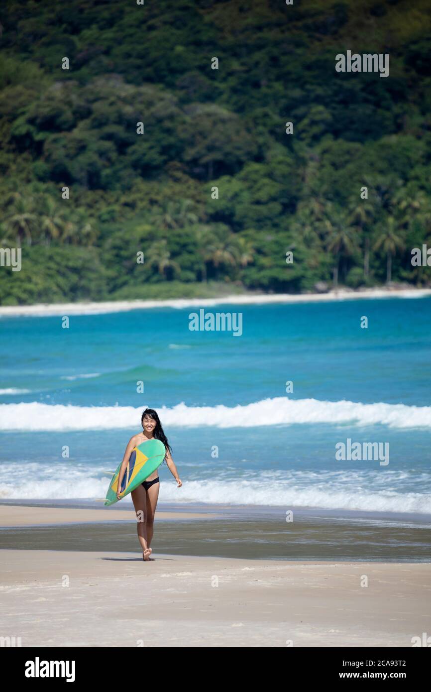 Foto de playa de un brasileño japonés (Nipo-brasileiro) en un bikini con una tabla de surf decorada con la bandera brasileña, Brasil, América del Sur Foto de stock
