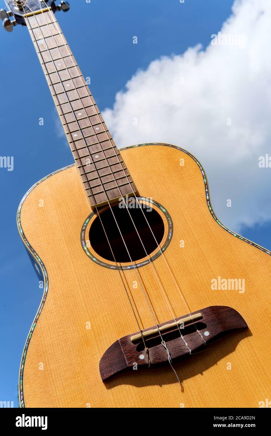 Guitarra acústica de barítono ukulele sostenida hasta el cielo azul  brillante con las nubes mullidas Fotografía de stock - Alamy