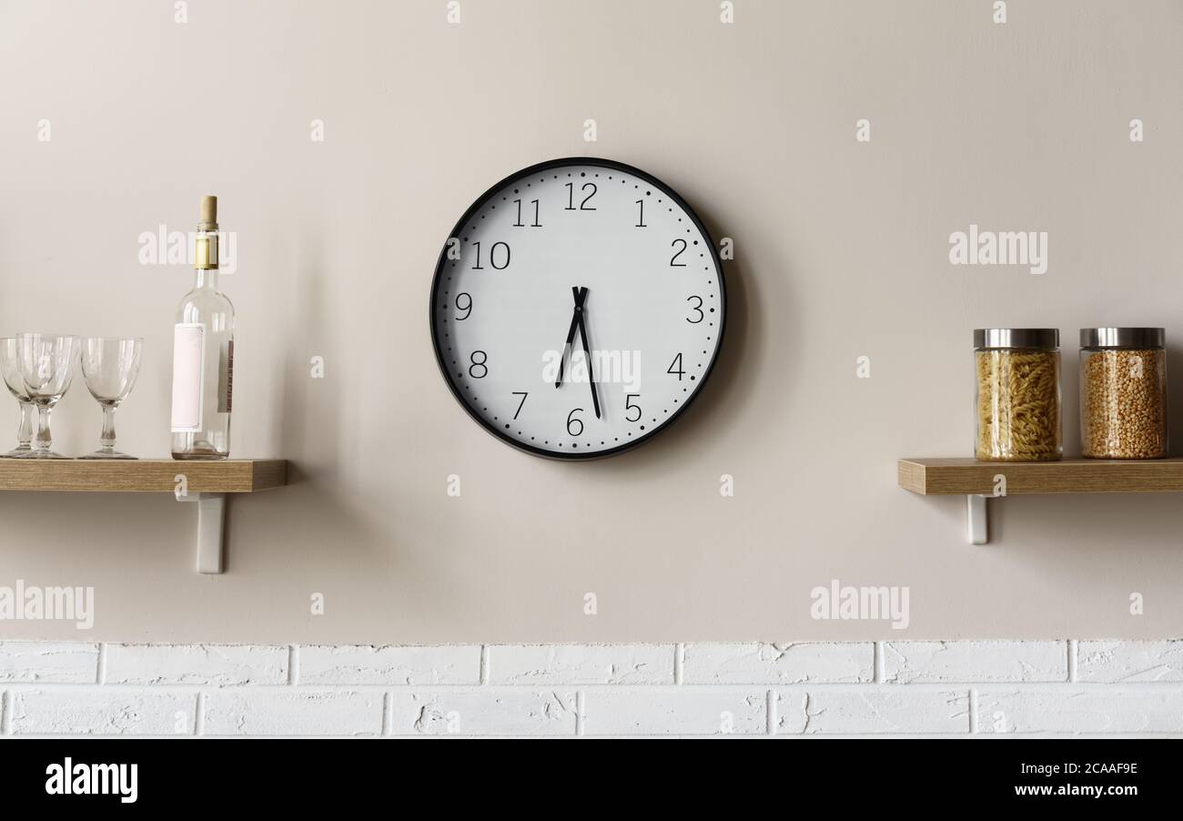 Reloj de pared redondo entre los estantes de madera de la cocina mostrando la hora Foto de stock