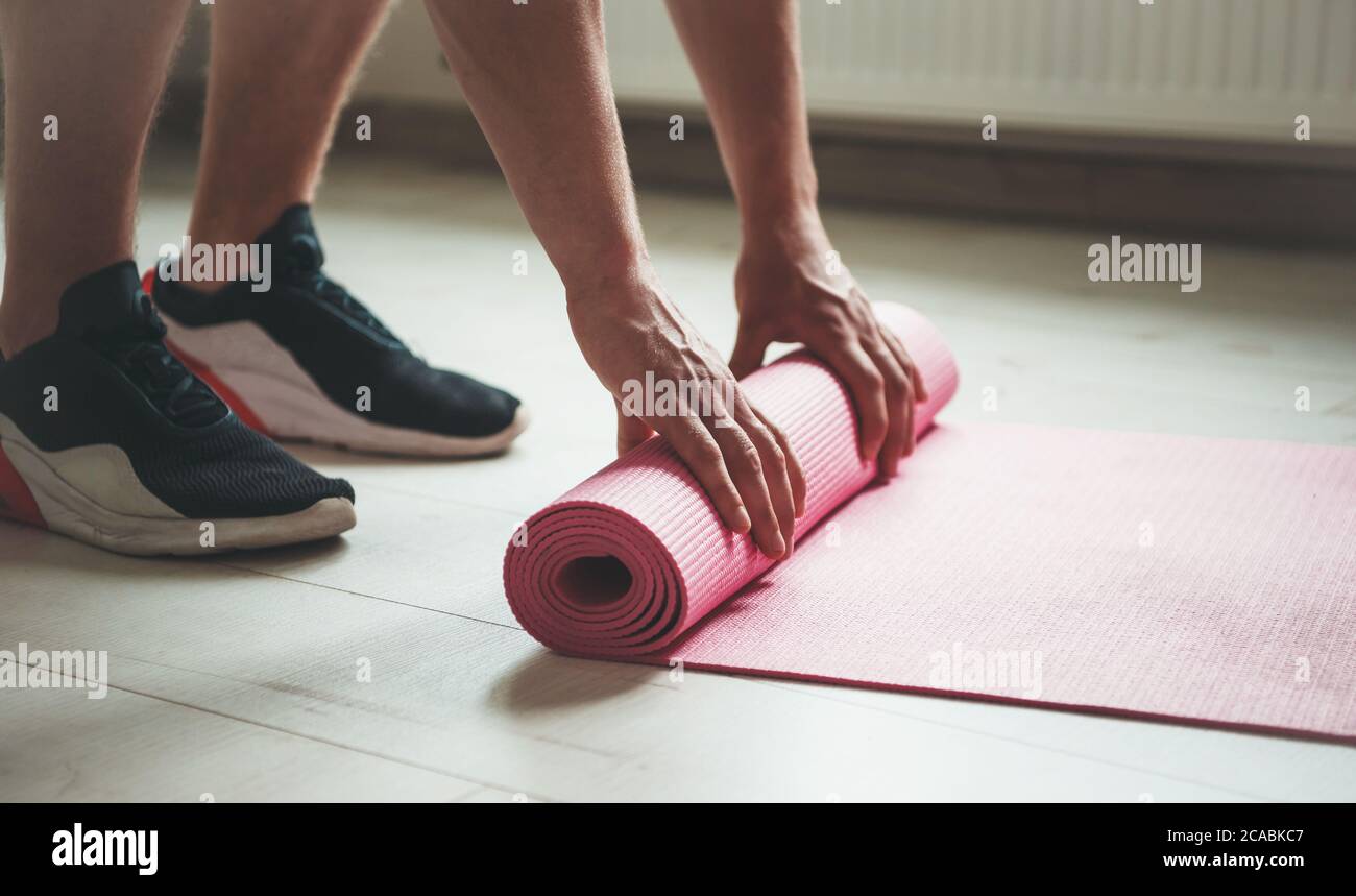 Vista lateral foto de una persona caucásica en sportswear terminando su procedimiento de yoga y recogiendo la alfombra Foto de stock
