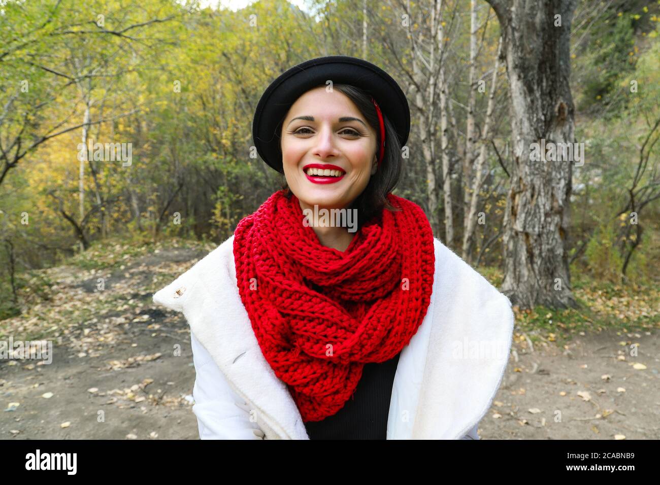 Hermosa mujer joven en un blanco, bufanda roja de ganchillo y sombrero negro. Retrato sonriente al aire libre Fotografía de stock - Alamy