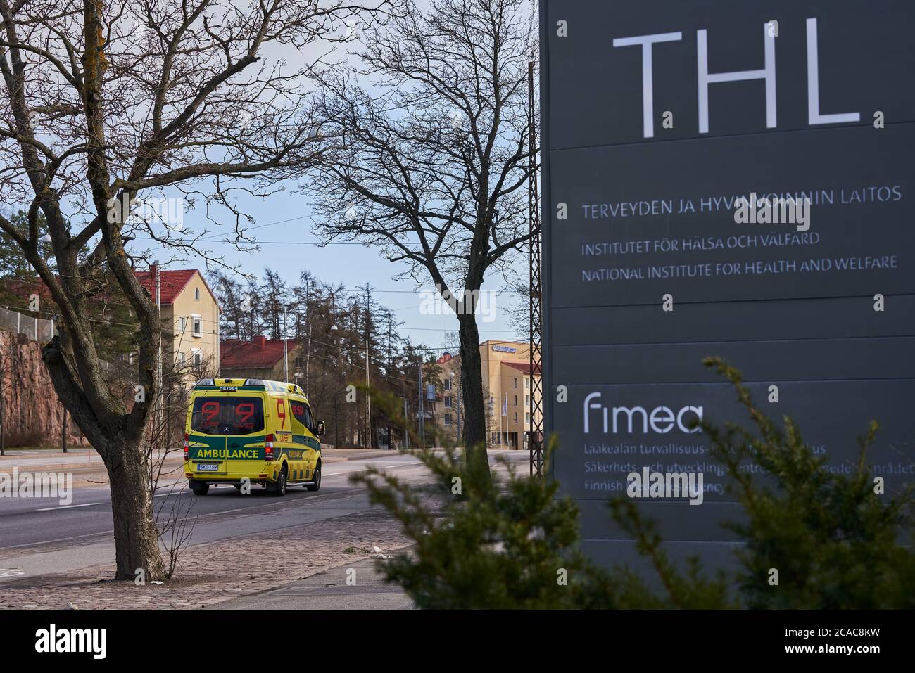 Helsinki, Finlandia - 4 de abril de 2020: Señal al aire libre del Instituto Nacional para la Salud y el Bienestar (THL) (finlandés) con una ambulancia que pasa por Mannerh Foto de stock