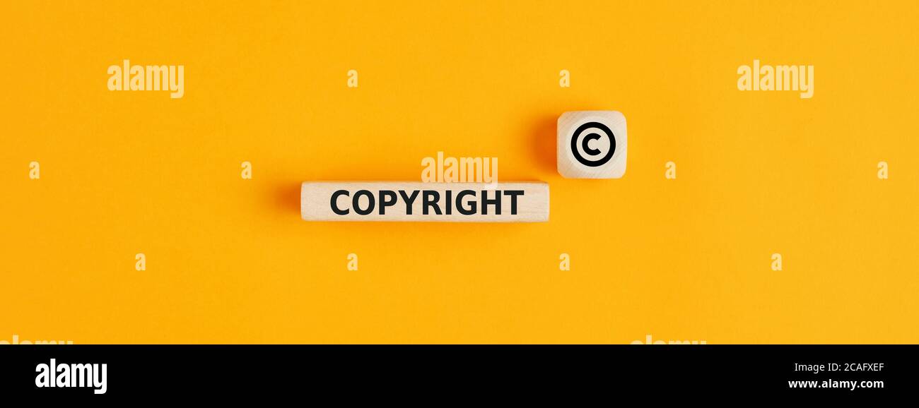 La palabra copyright y el símbolo de copyright en bloques de madera sobre fondo amarillo. Concepto de patente o protección del derecho de autor. Foto de stock