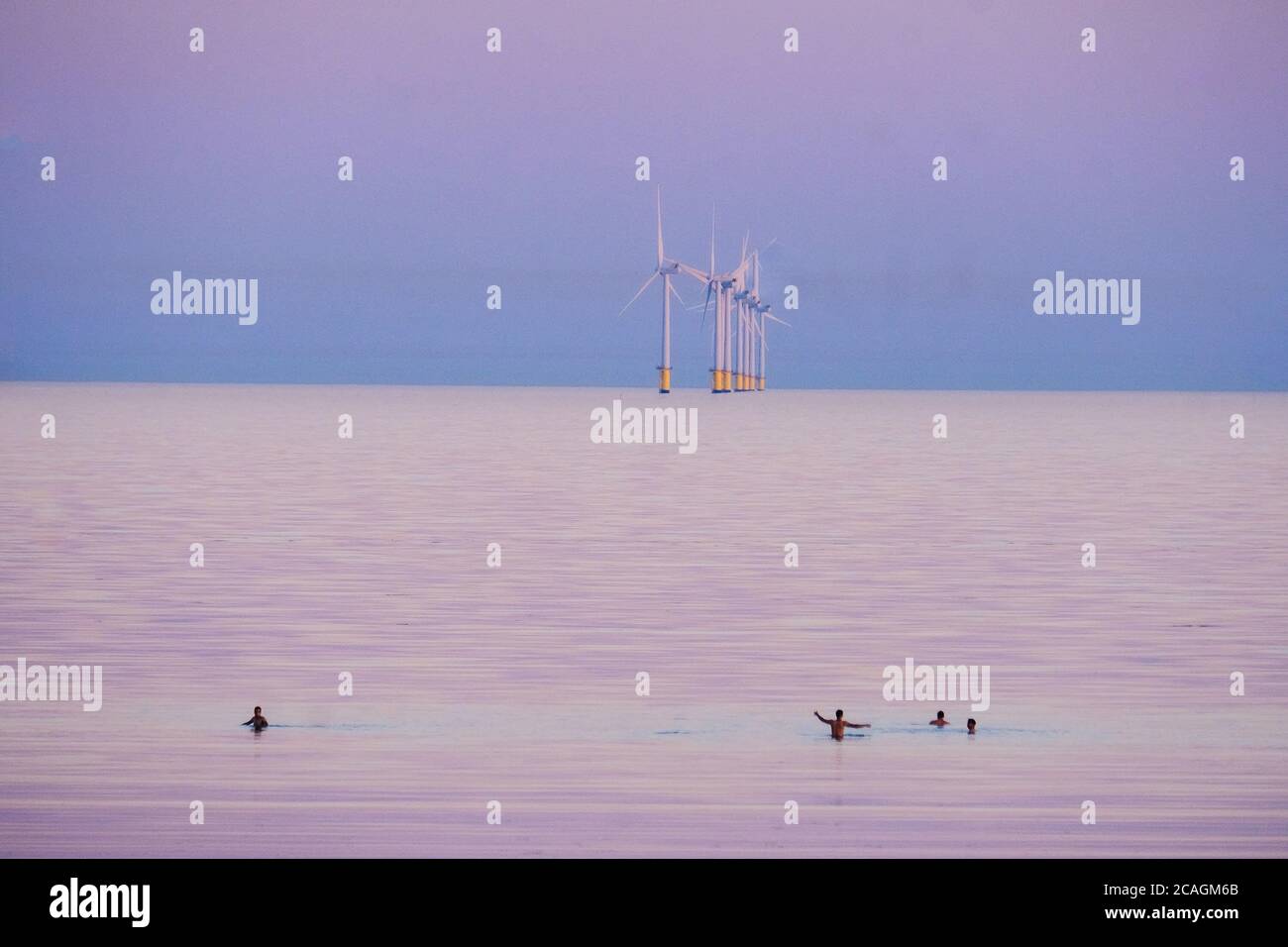 Worthing Beach, Worthing, Reino Unido. 6 de agosto de 2020. La gente nade en el mar tranquilo mientras el sol se pone brillando en una cálida noche de verano. El Parque Eólico de Rampion se puede ver en el fondo, 13km-16km de la costa. Imagen de crédito: Julie Edwards/Alamy Live News Foto de stock