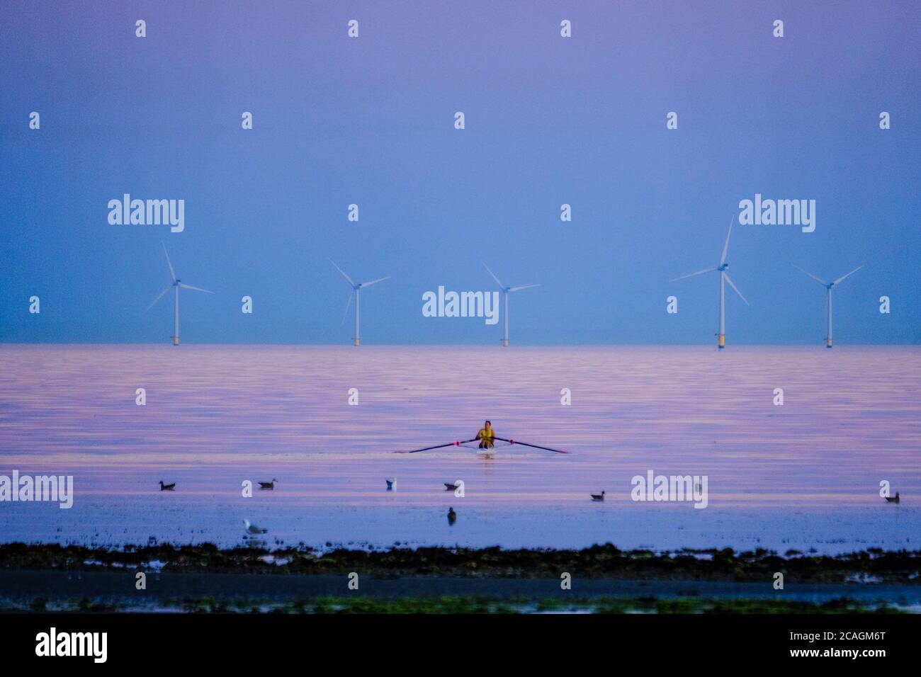 Worthing Beach, Worthing, Reino Unido. 6 de agosto de 2020. Un rozador atraviesa el mar tranquilo mientras el sol se pone emitiendo un cálido resplandor en una cálida noche de verano. El Parque Eólico de Rampion se puede ver en el fondo, 13km-16km de la costa. Imagen de crédito: Julie Edwards/Alamy Live News Foto de stock