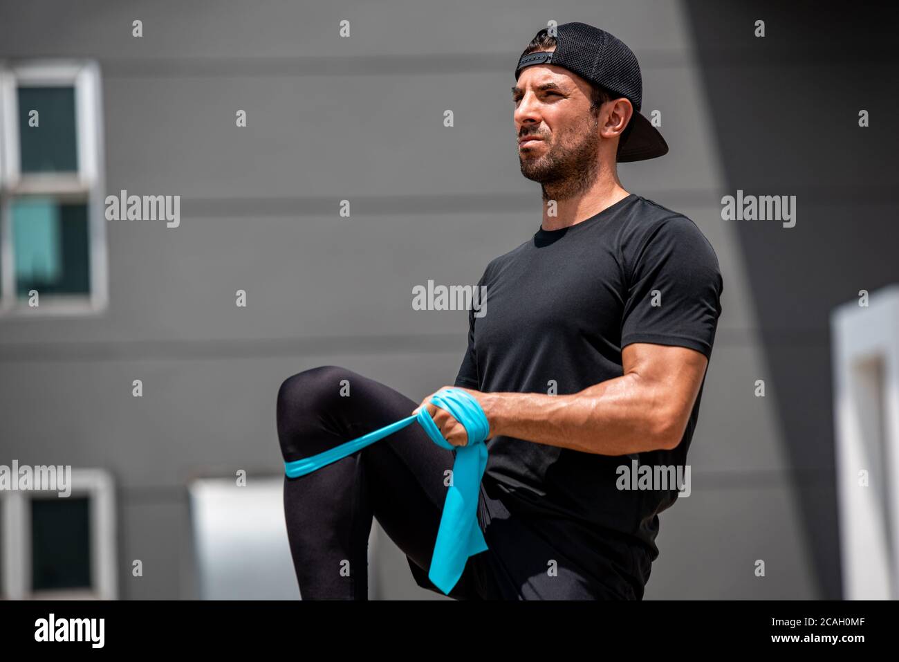 Hermoso hombre deportivo latino calentándose con la banda de resistencia antes haga ejercicio al aire libre en casa Foto de stock