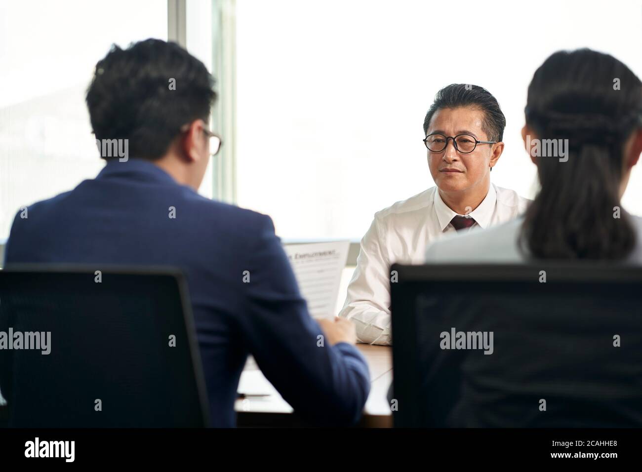 un hombre de negocios asiático más viejo que busca trabajo siendo entrevistado por jóvenes ejecutivos de recursos humanos Foto de stock