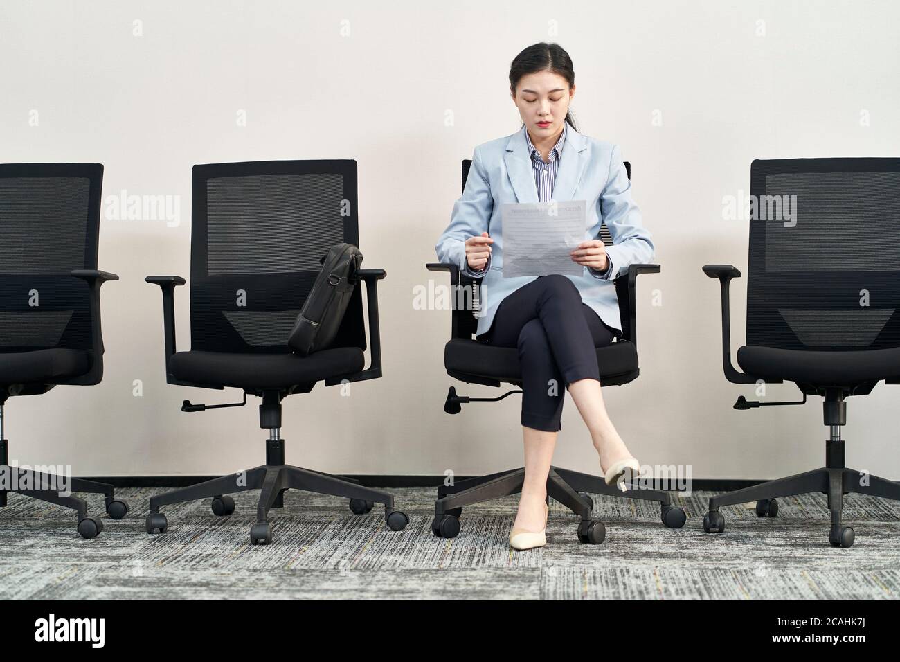joven mujer asiática aplicadora sentada en silla preparándose para la entrevista mientras espera en línea Foto de stock