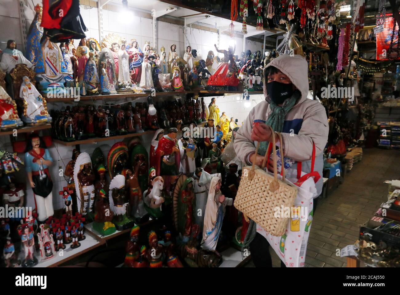 Una mujer compra en una tienda que vende artículos religiosos católicos  fuera de la iglesia de San Cayetano (San Cajetán), patrona del trabajo y el  pan, durante su día de fiesta, en