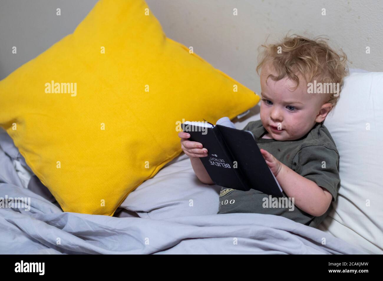 Denver, Colorado - Hendrix Hjermstad, de dos años, tiene un libro boca abajo mientras pretende leer. Foto de stock