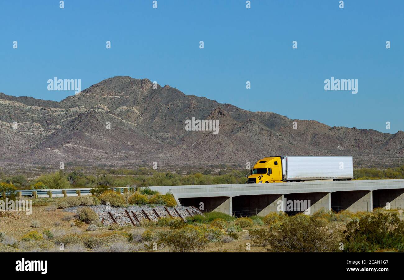 Gran equipo de largo recorrido semi camión con dos camas planas semirremolques transportando en la carretera sinuosa con el puente alrededor La roca de montaña en EE.UU Foto de stock