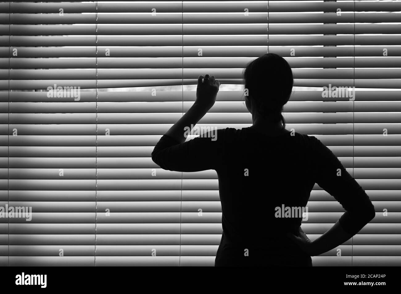 Mujer adulta de edad media mirando a través de una cortina veneciana. Concepto foto de persona que tiene Pistanthrofobia y Agorafobia, un sospechoso per Foto de stock