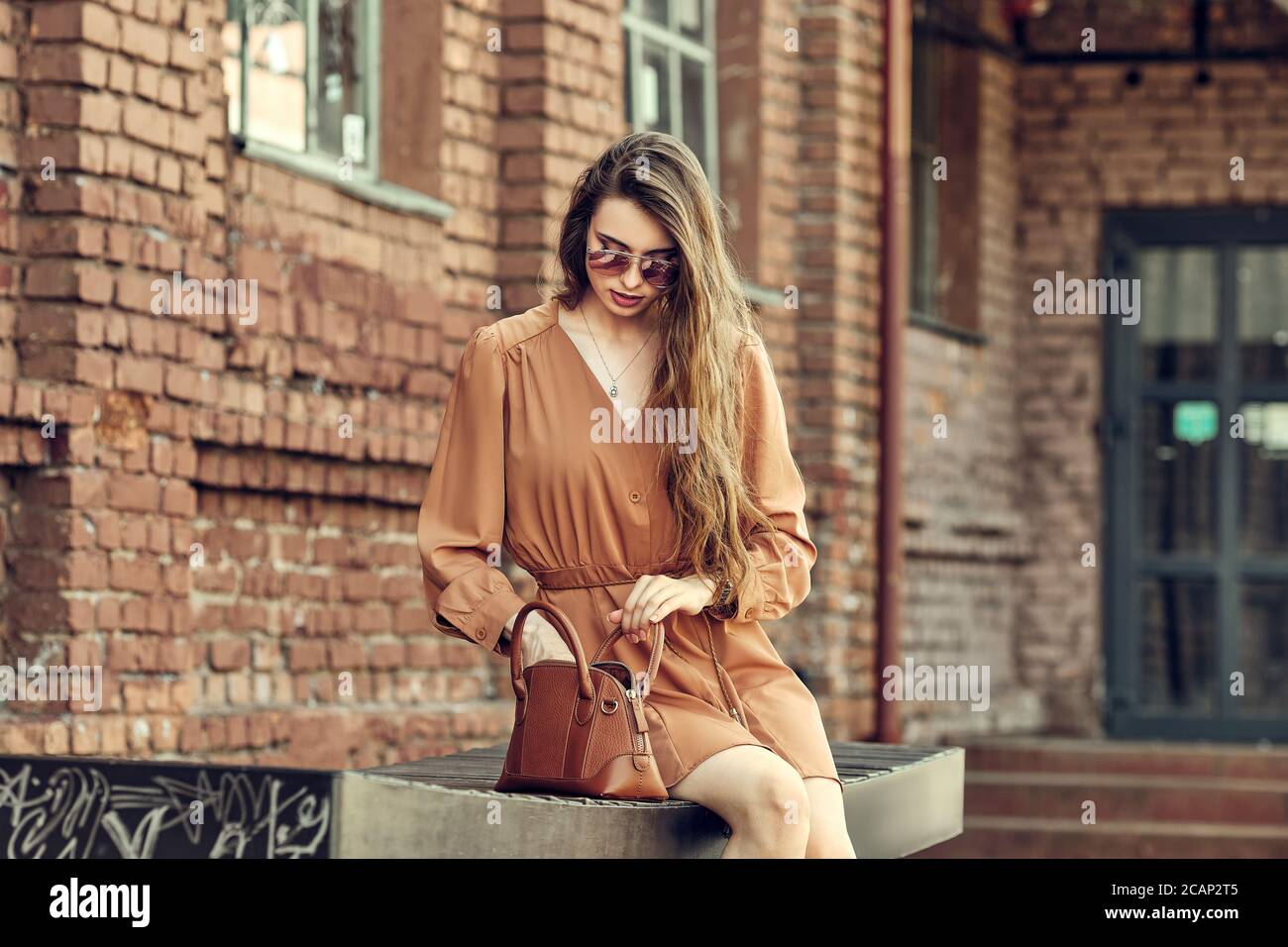 Mujer joven y bonita con vestido corto sentada en el banco y en busca de un someting en bolsa Foto de stock