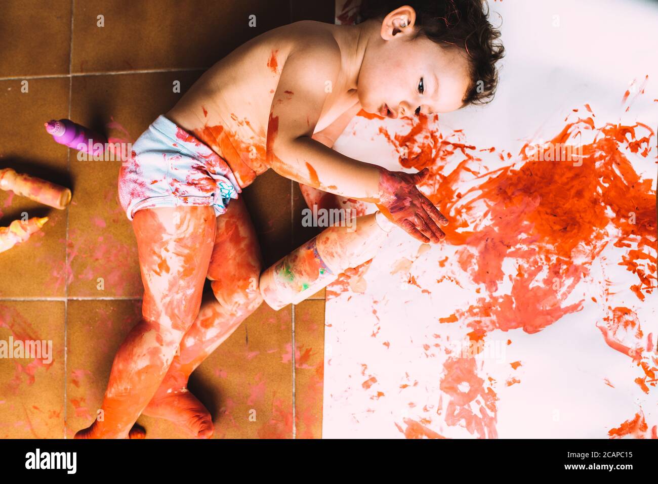 La niña creativa pinta en el suelo con la pintura de los niños un dibujo abstracto de los bebés sin formas. Foto de stock