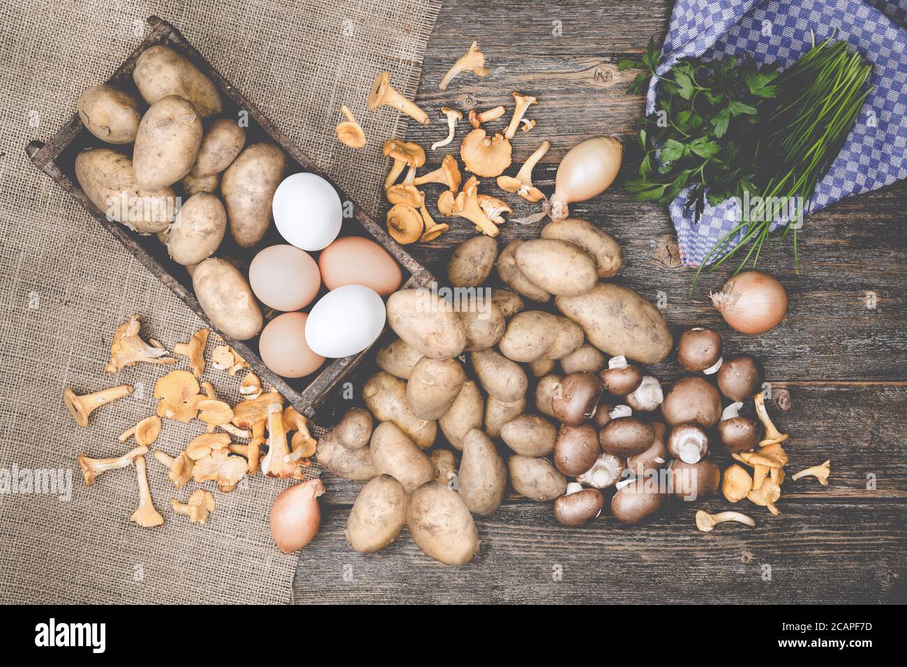Patatas, champiñones, huevos, parslex, cebollino y cebollas en una mesa de modden con arpillera Foto de stock