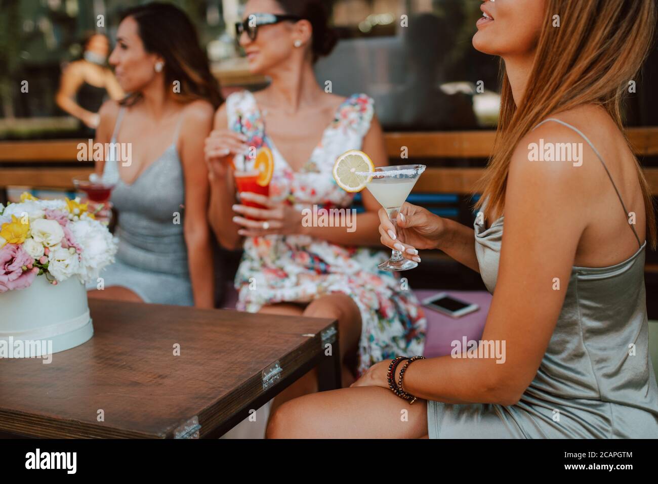 Tres hermosas mujeres caucásicas jóvenes en vestidos cortos de verano están  sentados y bebiendo cócteles en el café jardín. Niñas en fiestas Fotografía  de stock - Alamy