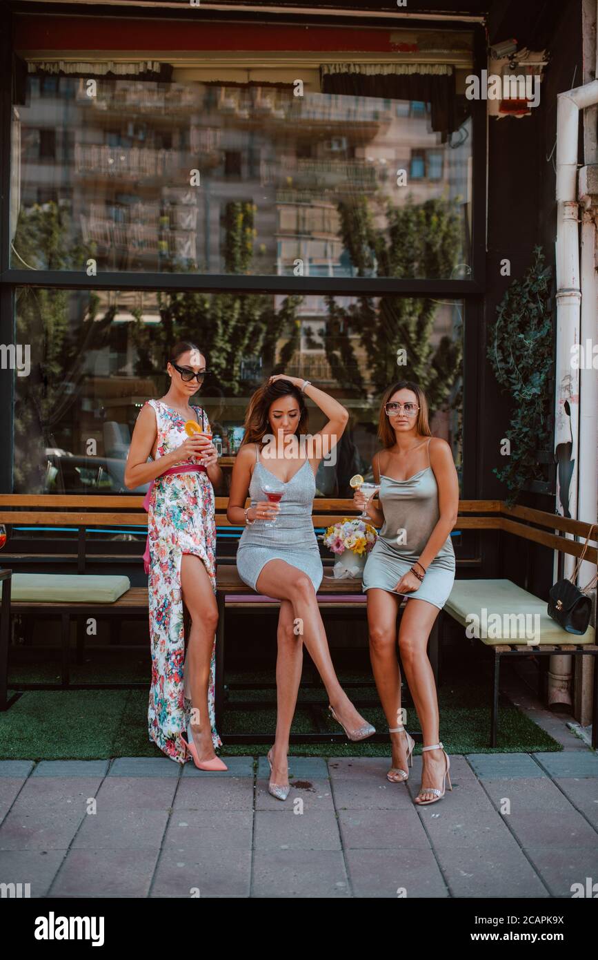 La longitud completa de tres mujeres jóvenes caucásicas hermosas en vestidos cortos de verano están bebiendo cócteles en un jardín café. Chicas de fiesta Fotografía de stock - Alamy La longitud completa de tres mujeres jóvenes caucásicas hermosas en vestidos cortos de verano están bebiendo cócteles en un jardín café. Chicas de fiesta Fotografía de stock - Alamy