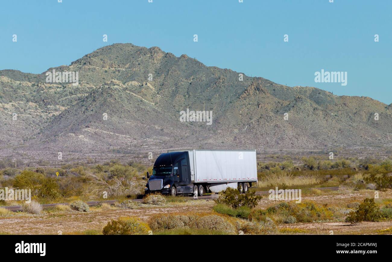 Vista lateral del transporte de la flota de semi camiones de gran plataforma carga en semirremolque largo en la carretera plana en Montaña EE.UU Foto de stock