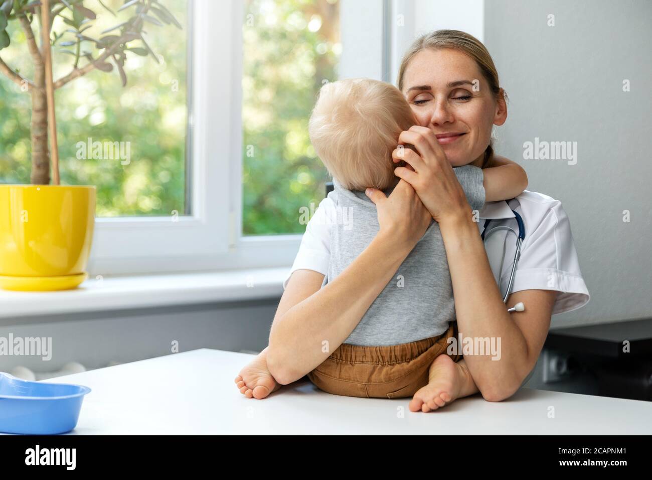 amable pediatra agradable abraza al niño paciente en el consultorio de la clínica. empatía y amor a su concepto de trabajo Foto de stock