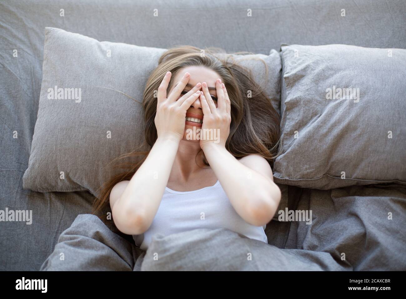 Vista superior de una chica bonita acostada en la cama y la cubierta su cara con las manos Foto de stock