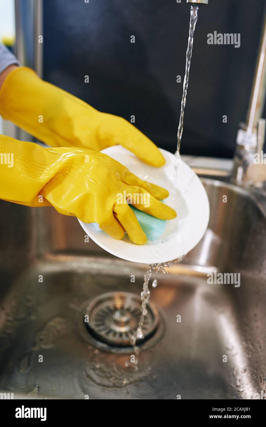 Imagen de primer plano de ama de casa en guantes de goma lavando platos y. enjuague con agua del grifo Foto de stock