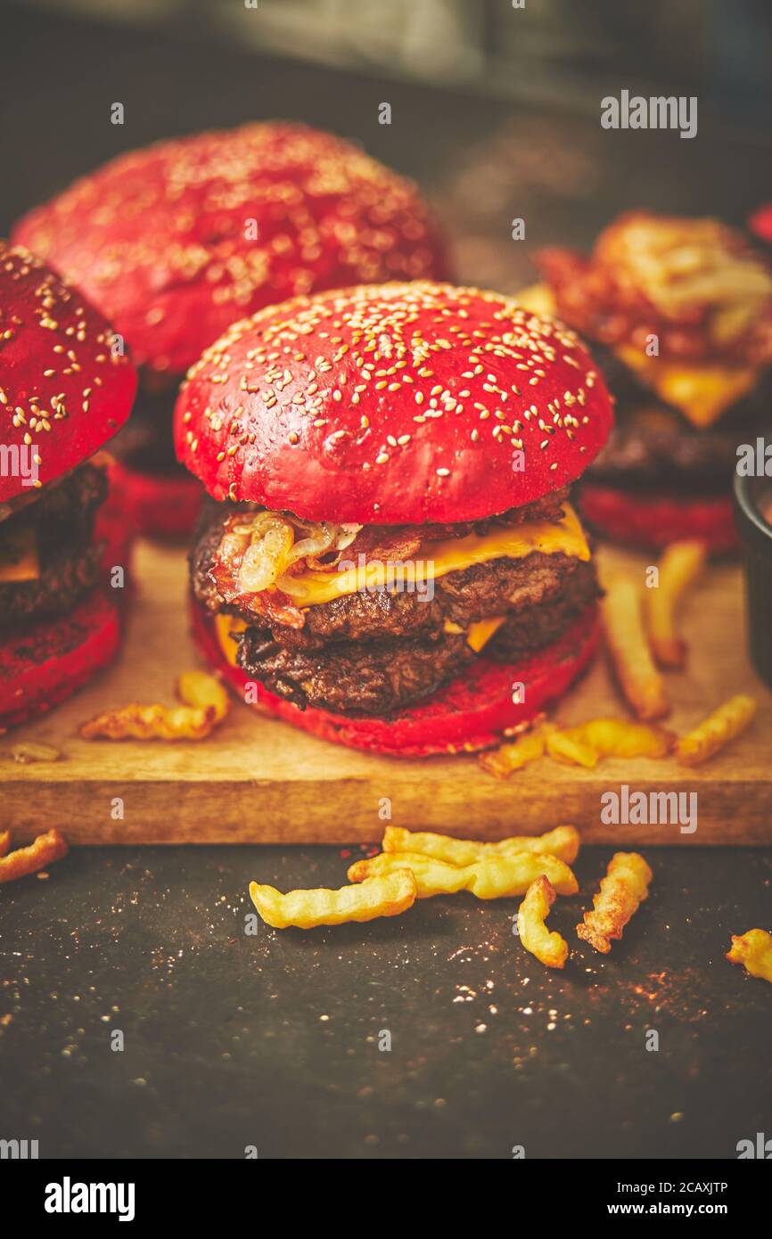 Un juego de bollo rojo casero deliciosas hamburguesas de carne de res, tocino, queso, cebolla a la parrilla en un oxidado oscuro Foto de stock