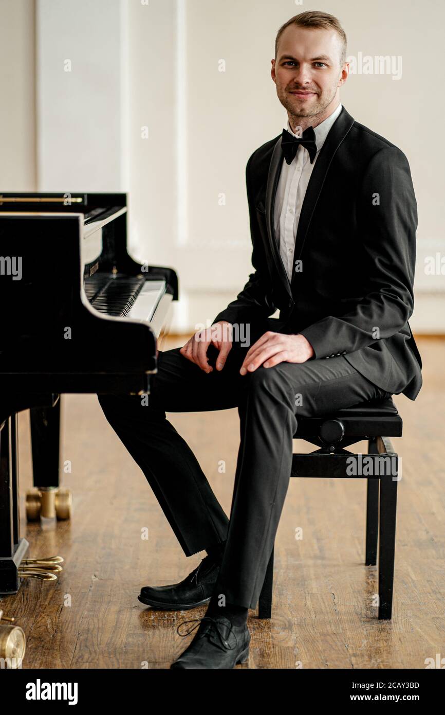 retrato de un joven pianista en traje elegante formal con pajarita, sentado  junto al piano de instrumentos clásico y mirando a la cámara Fotografía de  stock - Alamy