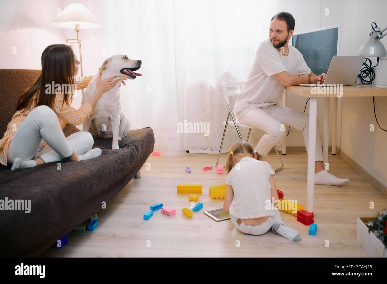 familia juntos en casa, pasar tiempo libre, vacaciones en la sala de estar, tener un descanso. Niño niña jugar con juguetes, mujer acariciando a su perro doméstico, mientras que hombre Foto de stock