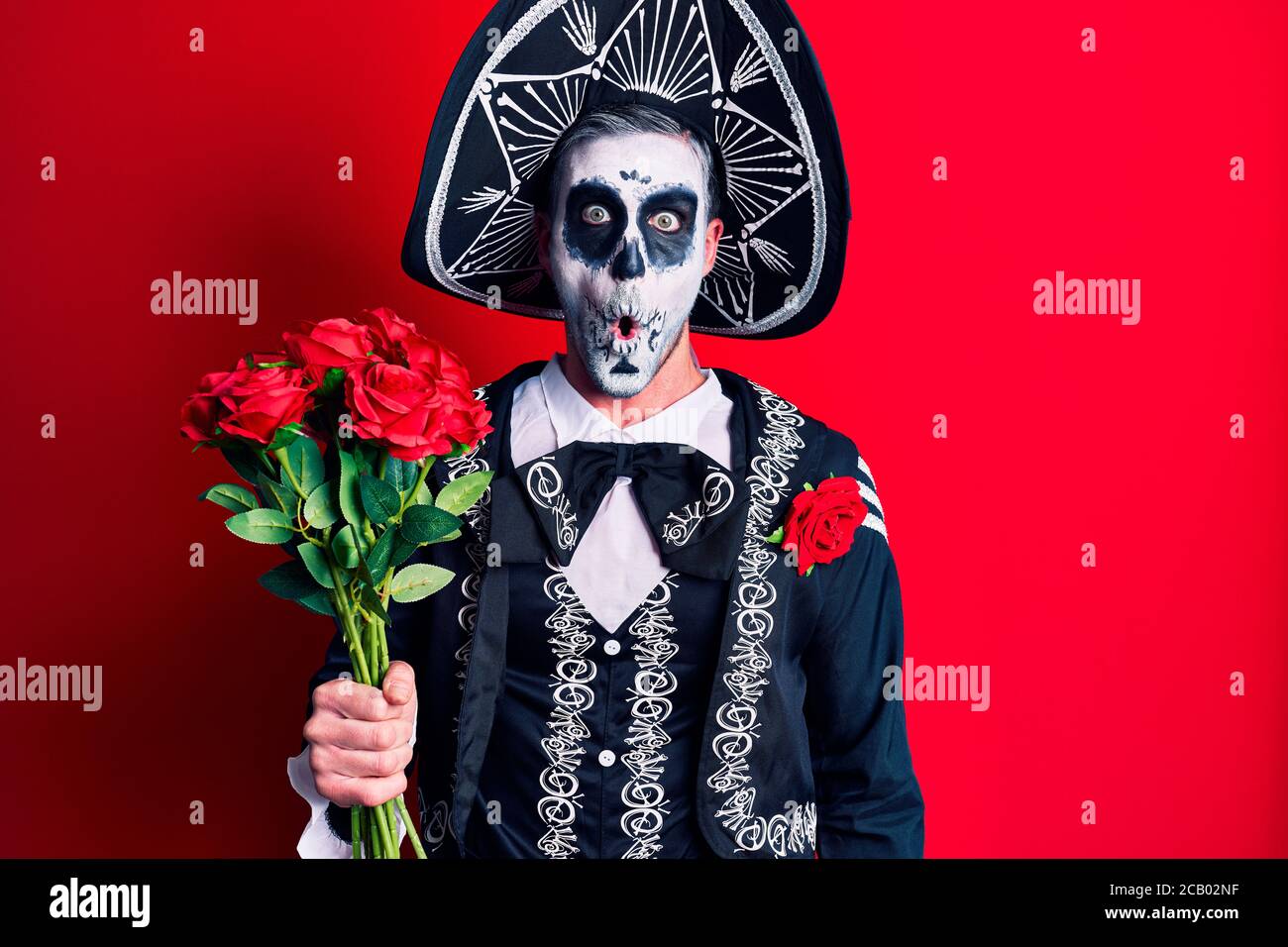 Hombre joven con el día mexicano de la muerte disfraz con rosas asustadas y  asombradas con boca abierta para sorpresa, la cara de incredulidad  Fotografía de stock - Alamy