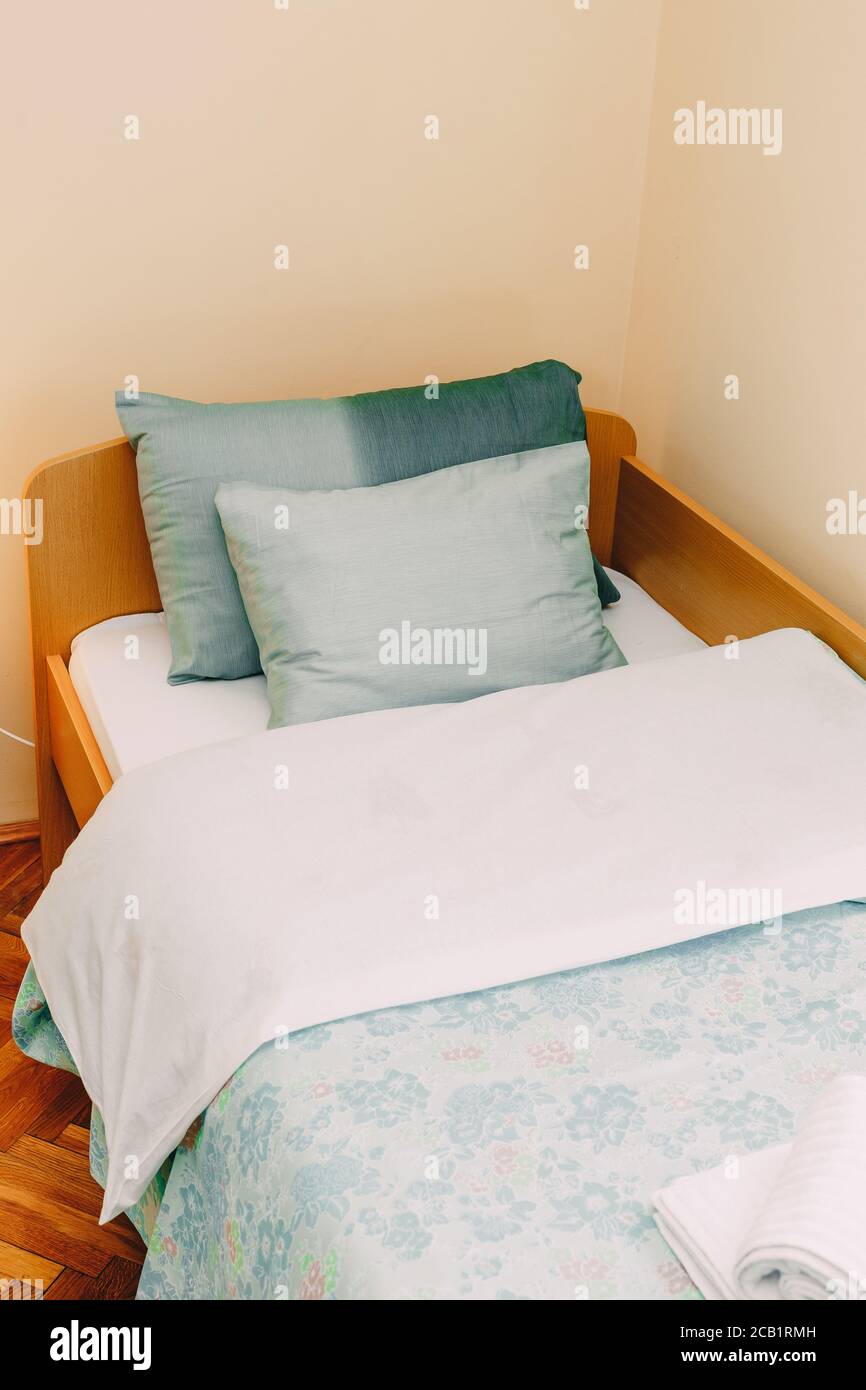 Una cama hecha con dos almohadas azules y una tabla lateral en una  habitación con paredes claras Fotografía de stock - Alamy