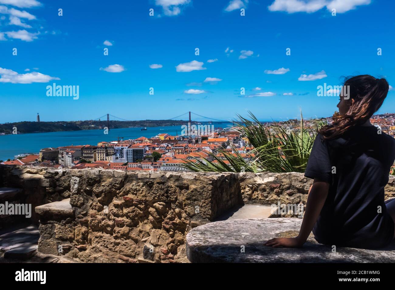 Vista de perfil de una adolescente mirando el paisaje urbano de Lisboa y el Ponte 25 de Abril en el fondo. Foto de stock