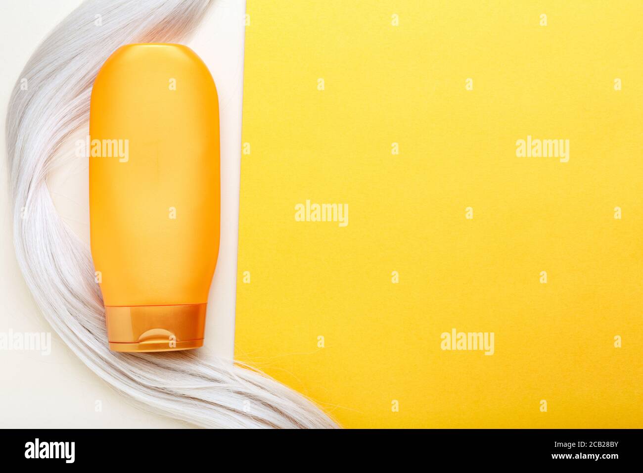 Shampoo botella de mascup hilo en el mechón de pelo rubio sobre fondo de color naranja. Champú de botella de naranja. Arriba ver copiar espacio.Cuidado del cabello cosméticos Foto de stock