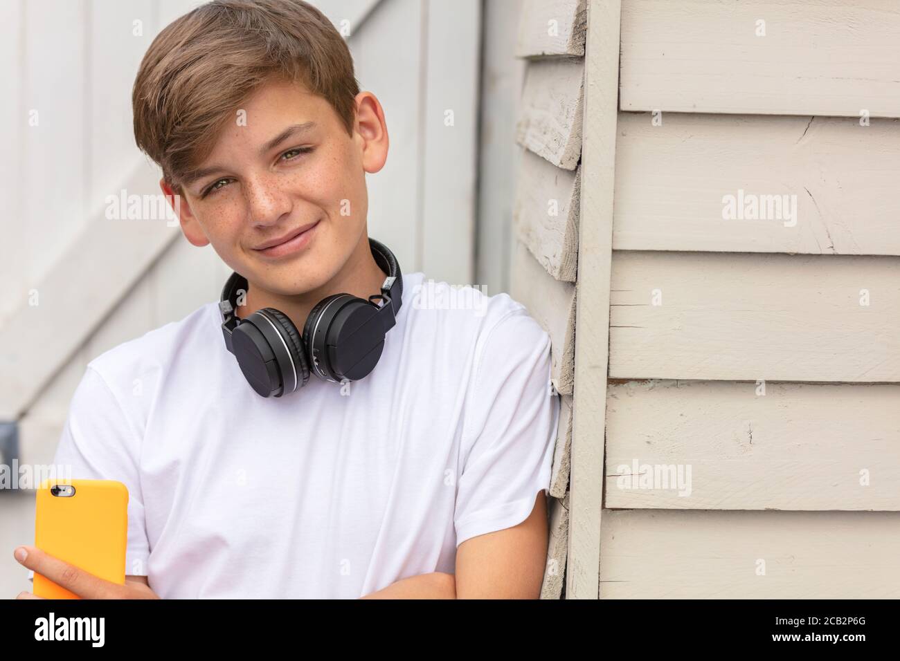 Niño adolescente adolescente niño adolescente fuera usando su célula móvil teléfono y auriculares inalámbricos bluetooth para redes sociales o música Foto de stock