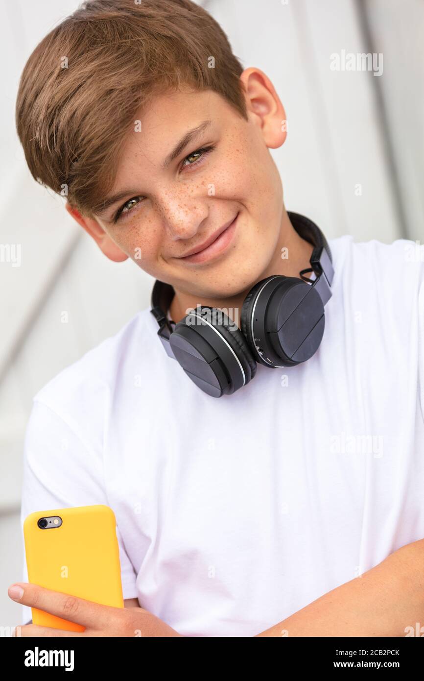 Niño adolescente adolescente niño adolescente fuera usando su célula móvil teléfono y auriculares inalámbricos bluetooth para redes sociales Foto de stock