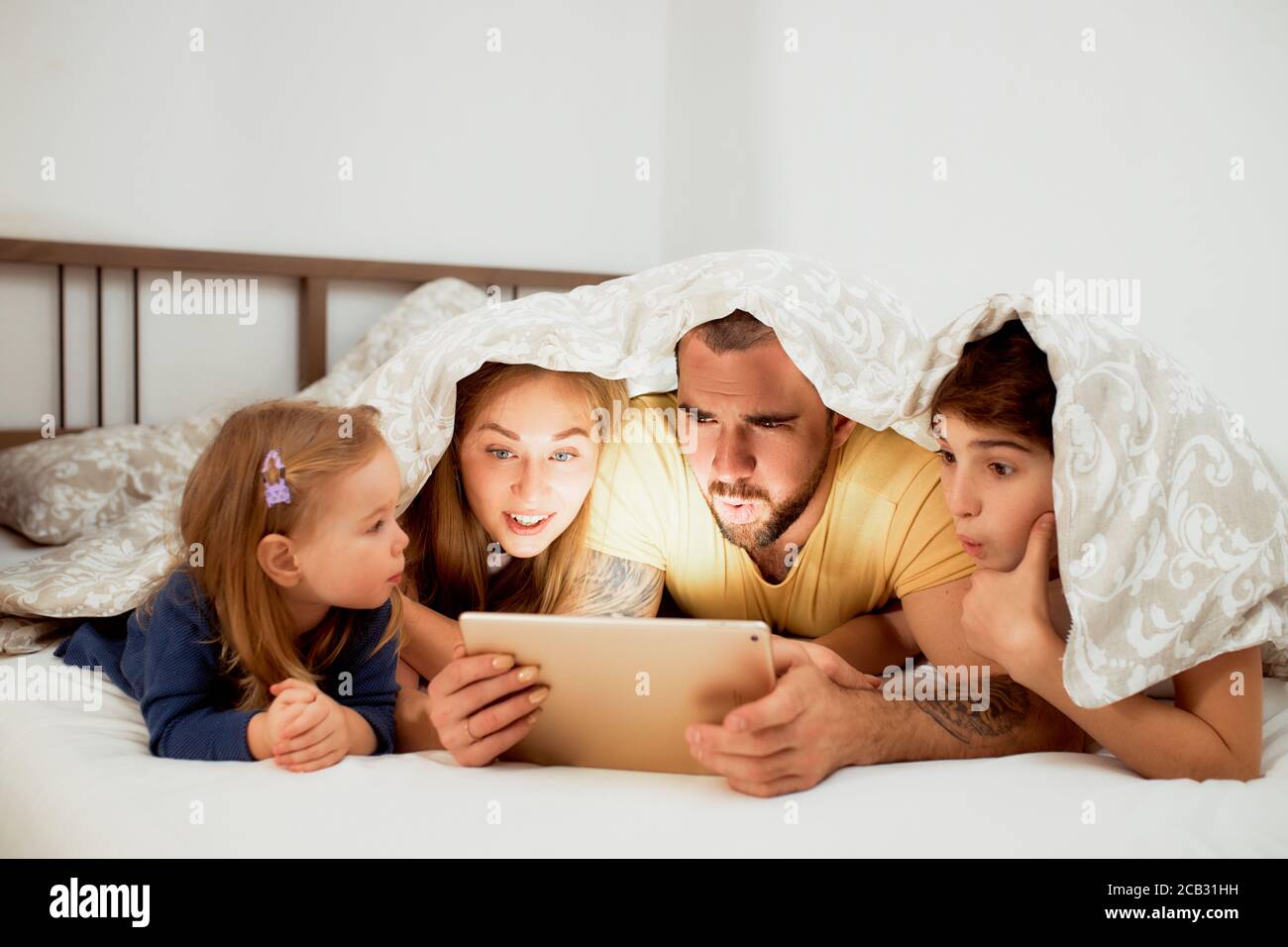 familia caucásica, madre sorprendida padre hijo e hija mirar la pantalla de  la tableta, viendo una película o video interesante, tumbado bajo el  edredón en la cama Fotografía de stock - Alamy