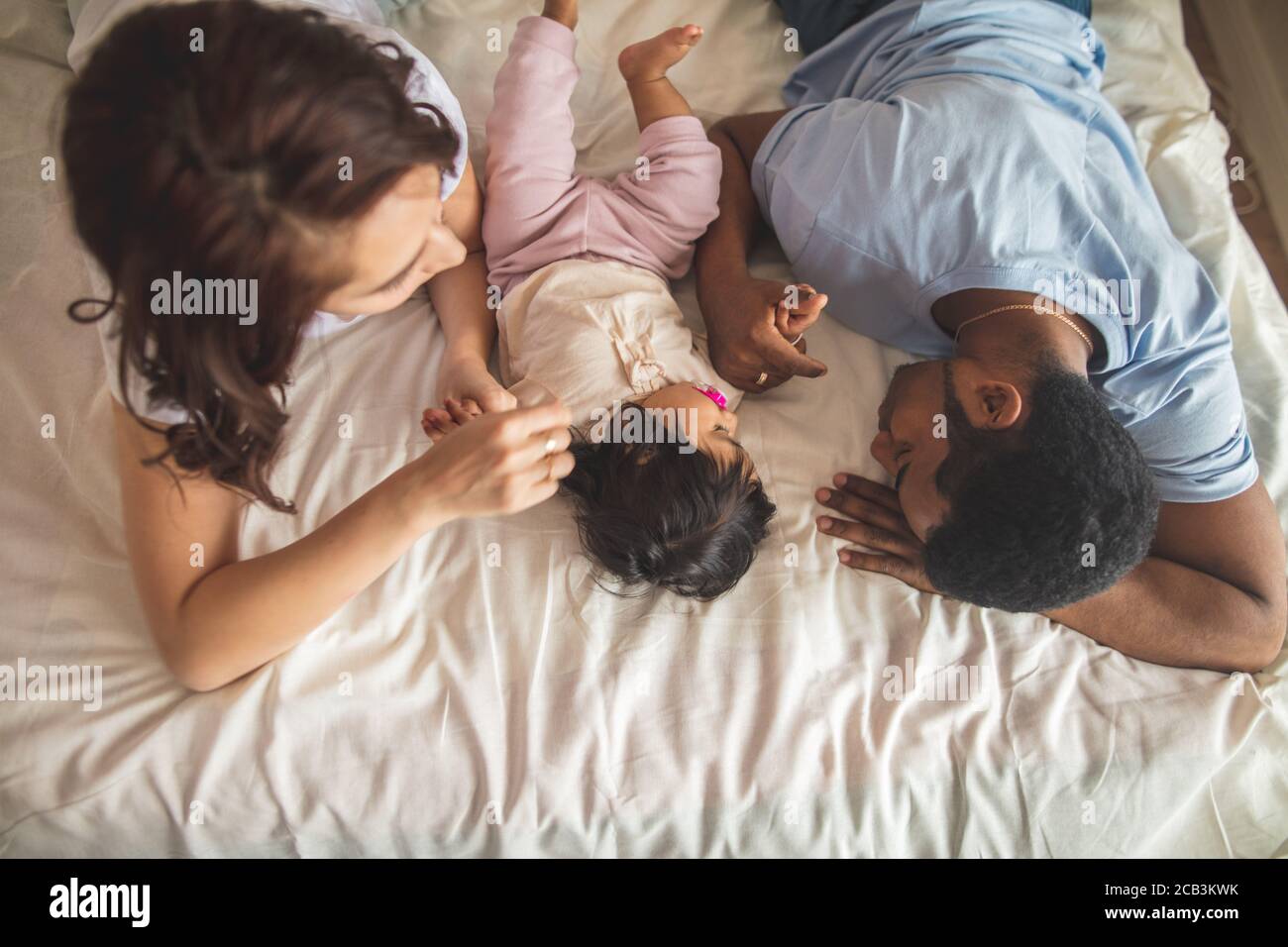 Feliz padre joven, madre y lindo bebé tumbado en la cama, foto de la vista superior. Tiempo libre y libre Foto de stock