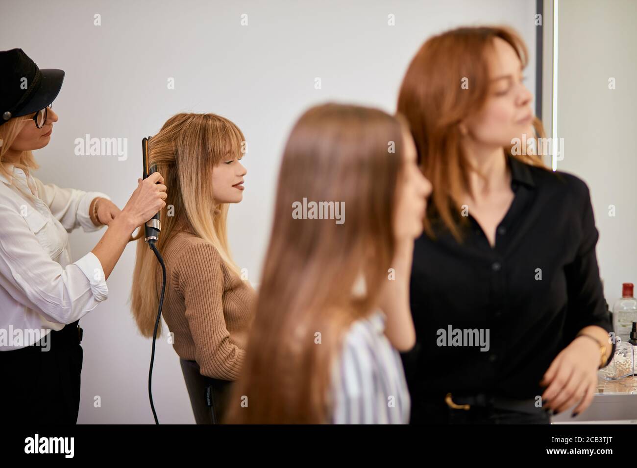 La moderna peluquería tidies el pelo largo de los clientes jóvenes, haciendo el pelo en la víspera de las vacaciones. Transformación completa en salón de belleza Foto de stock