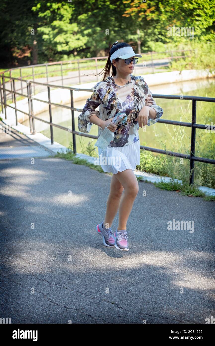 Un atractivo corredor asiático americano con una blusa y una falda plisada blanca alrededor del lago en Kissena Park, Flushing, Queens, Nueva York. Foto de stock