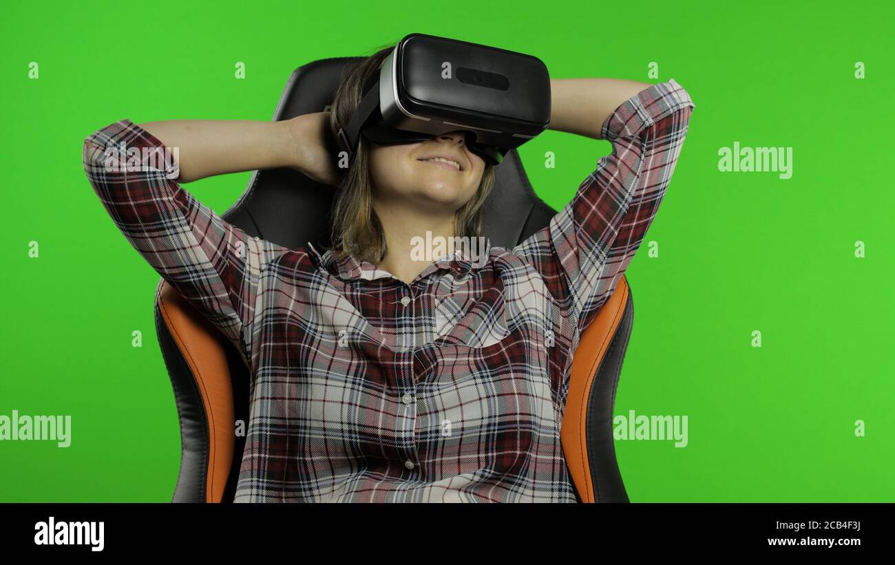 Mujer joven en el casco de auriculares VR juega el juego. Viendo vídeo de  realidad virtual en 3d 360. Mujer aislada sobre fondo verde de la clave de  croma en el estudio.