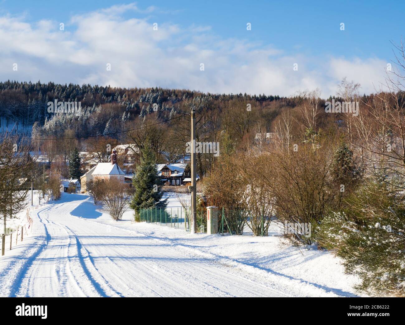 vista de invierno en el pueblo travnik con capilla, casa de madera y árboles, paisaje rural cubierto de nieve con en luzicke hory montaña Foto de stock