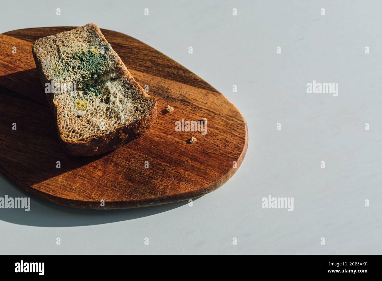 Molde sobre pan, un trozo de pan de centeno con molde blanco y verde sobre una tabla de madera. La fecha de mejor antes ha caducado. Foto de stock